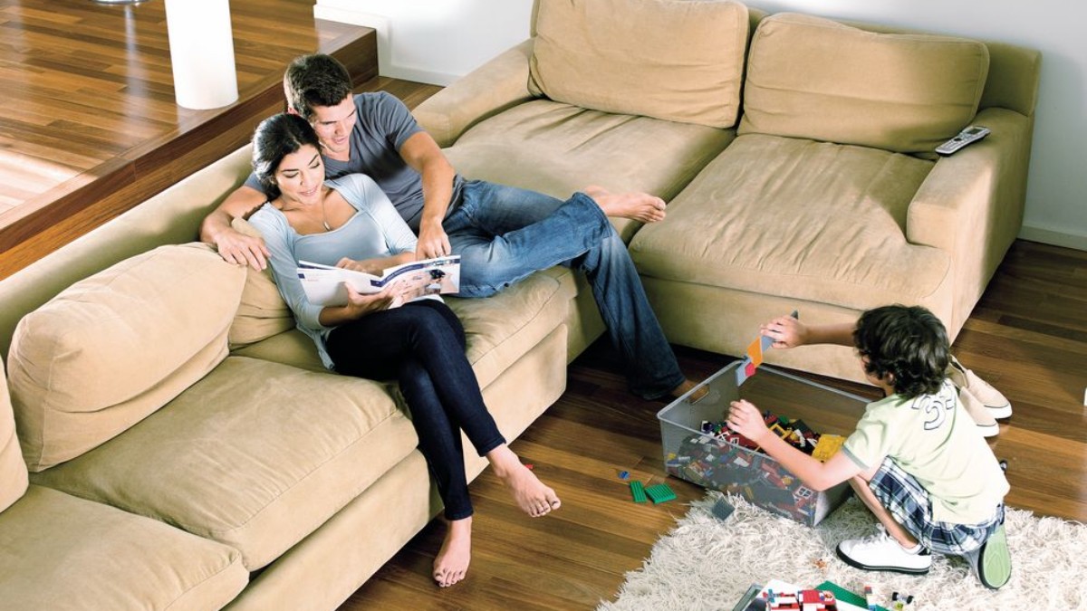 Un couple avec un enfant se trouve dans le salon et profite de la chaleur du plancher chauffant.
