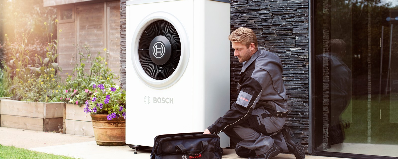 Un chauffagiste de Bosch se tient dans le couloir de l'immeuble et discute avec un couple de l'entretien de la pompe à chaleur.