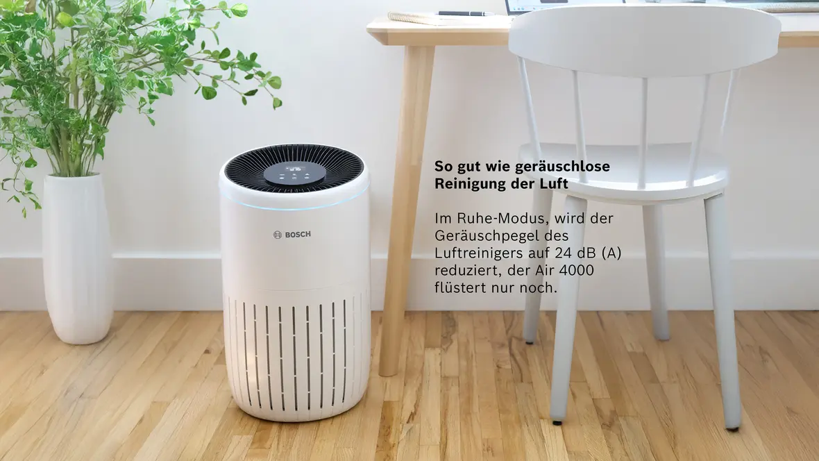 Bosch Air 4000 Luftreiniger im Raum neben Tisch und Stuhl, mit Text zur flüsterleisen Reinigung im Ruhe-Modus.