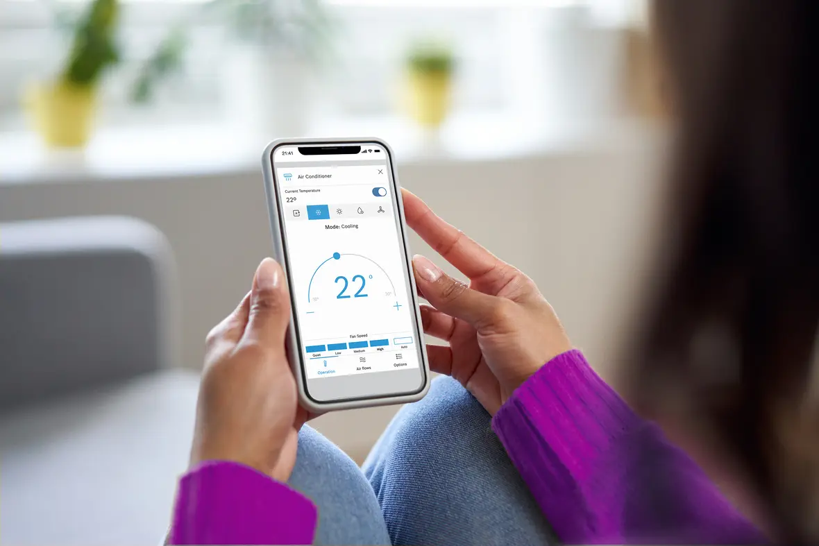 Frau steuert Bosch Climate 7000i Single-Split Klimagerät per App auf dem Smartphone, Temperatur auf 22 Grad eingestellt.