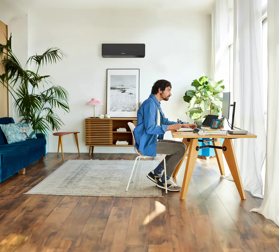 Mann arbeitet im Home Office, Bosch Climate 7000i Single-Split Klimagerät in Schwarz an der Wand über dem Schreibtisch.