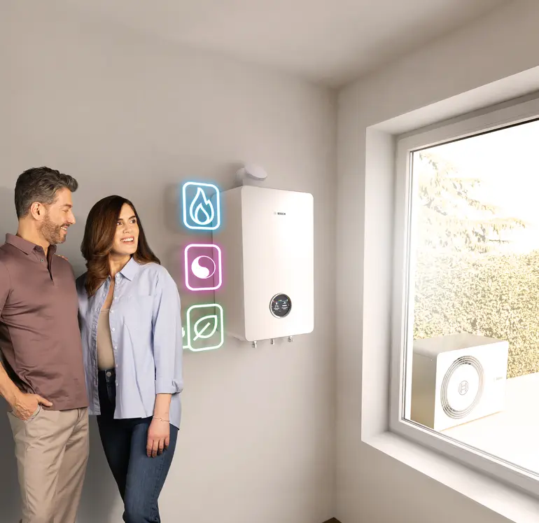 Paar steht vor Bosch All-in-One Heizung Compress Hybrid 5800i G, Icons für Gas, Hybrid und Wärmepumpe leuchten daneben.
