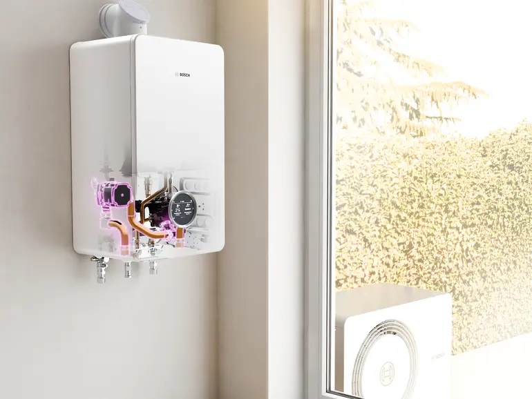 Bosch All-in-One Heizung Compress Hybrid 5800i G mit transparenter Front zeigt Blick ins Gerät mit inneren Komponenten, Außeneinheit im Garten sichtbar.