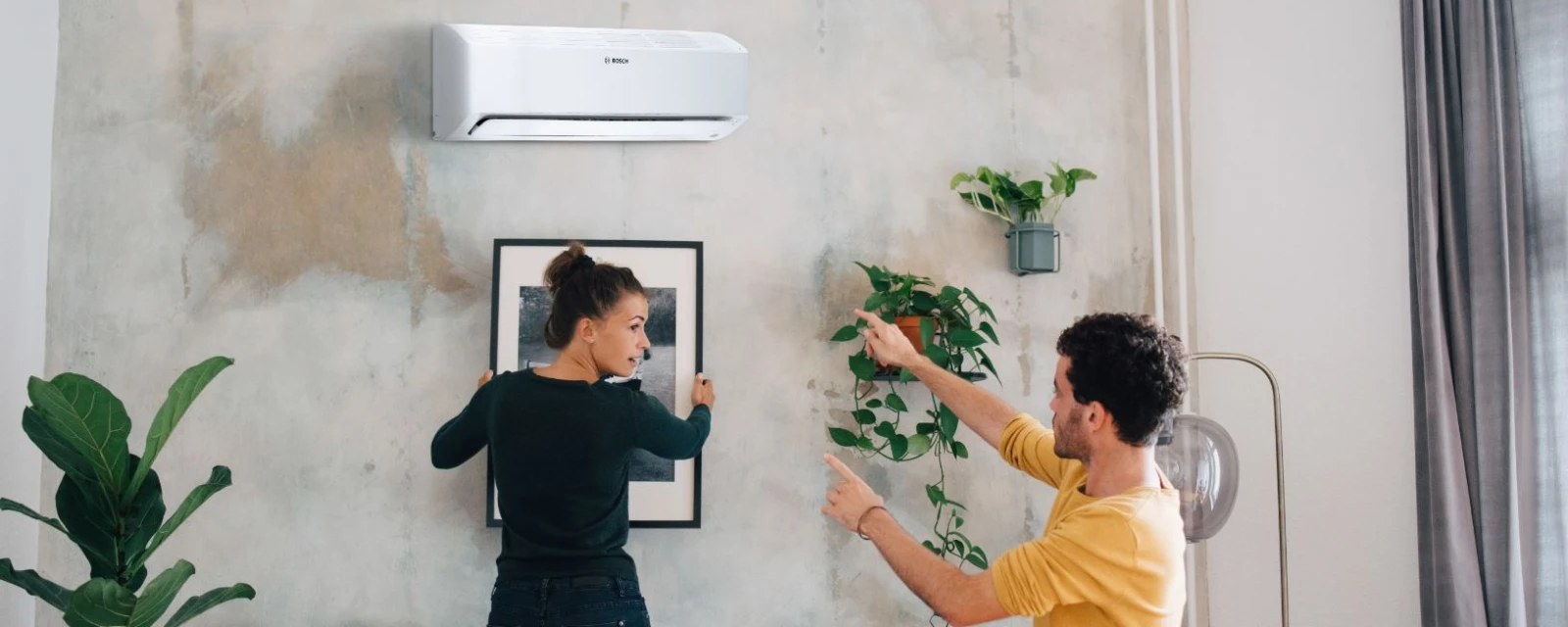 Bosch split air conditioner Climate Class 6000i hanging in the living room while a woman and a man hang a picture below.