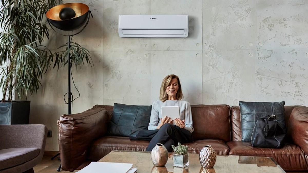 Woman sitting on the sofa with a tablet in her hand, Bosch Climate Class 6000i hanging on the wall in the background. Woman sitting on the sofa with a tablet in her hand, Bosch Climate Class 6000i hanging on the wall in the background.