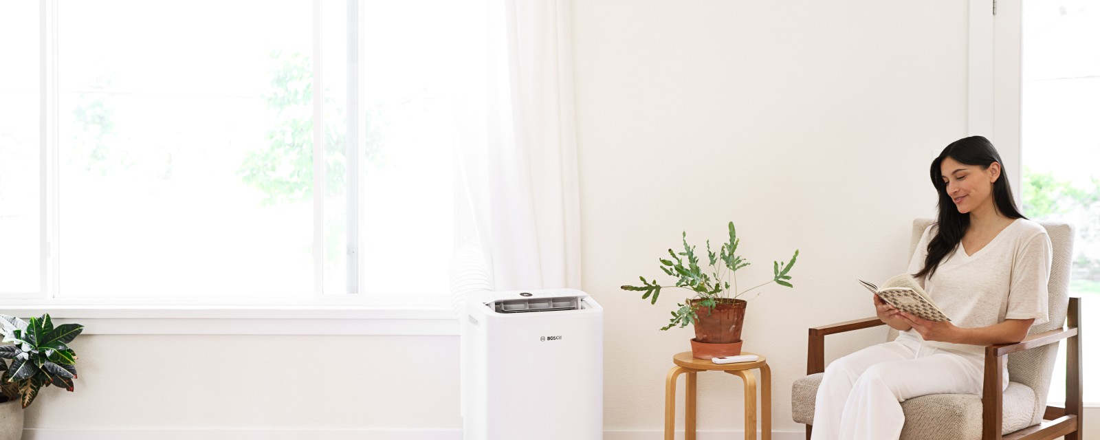 Woman sitting in a chair reading book while enjoying the cool air of Bosch mobile air conditioner.