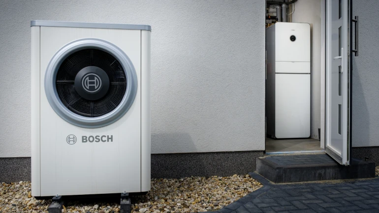 În fața unei case se află o pompă de căldură modernă de la Bosch cu un COP ridicat.