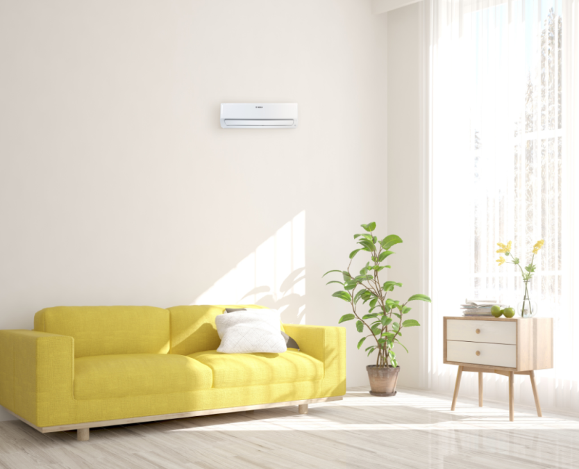 The new Bosch Climate Class 6000i split air conditioner hangs in a living room with yellow couch and houseplant