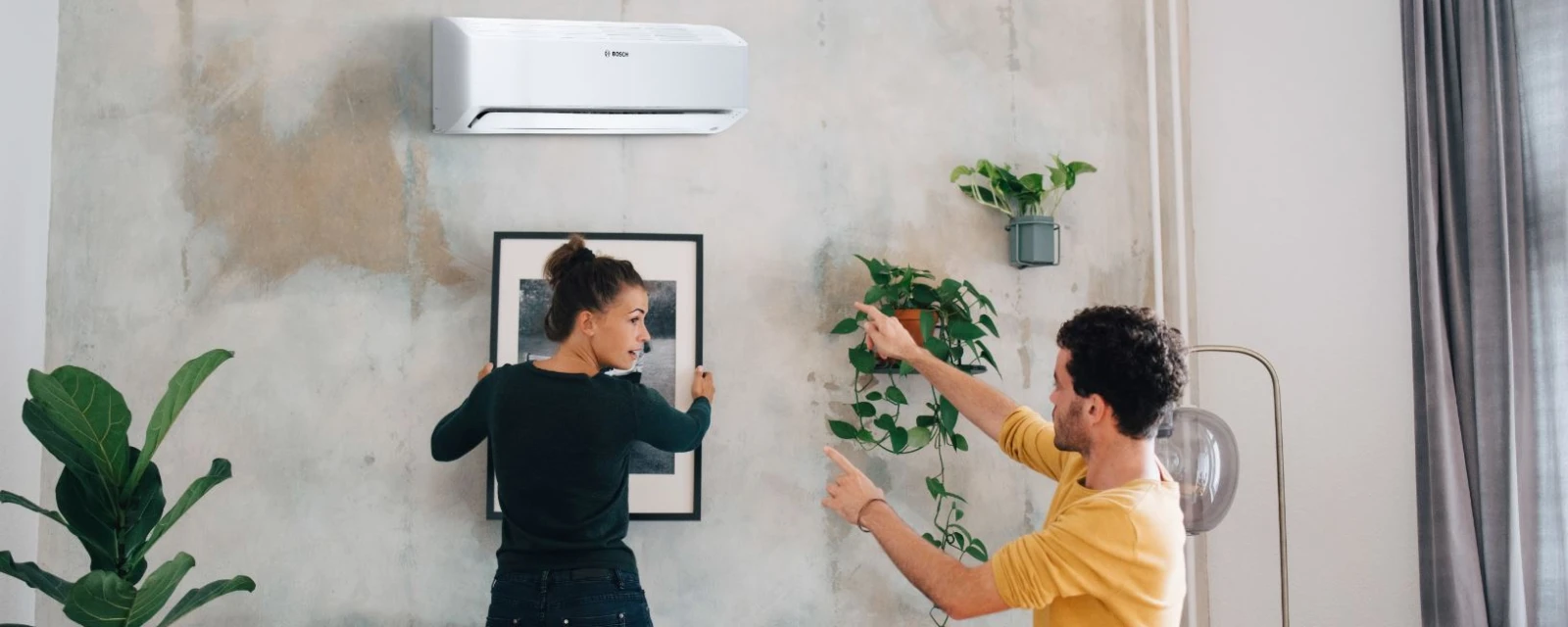 Bosch split air conditioner Climate Class 6000i hanging in the living room while a woman and a man hang a picture below.