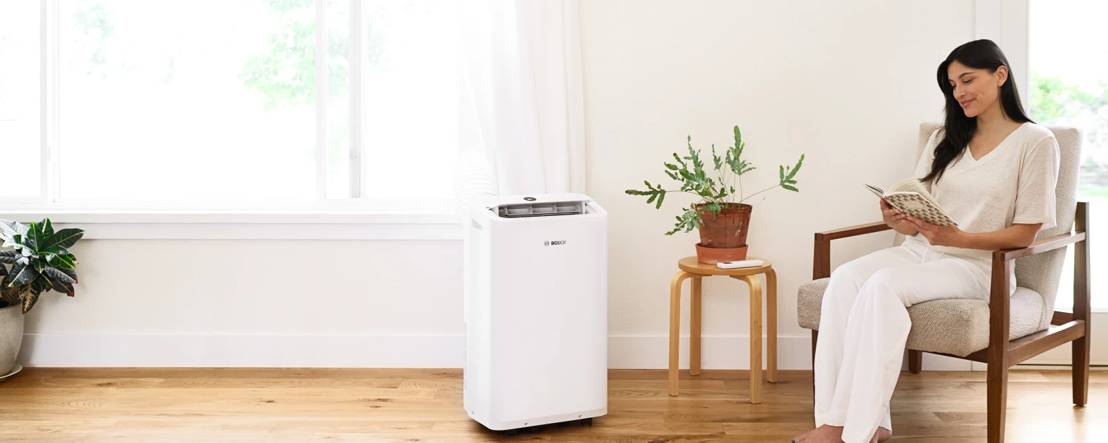 Woman sitting in a chair reading book while enjoying the cool air of Bosch mobile air conditioner.