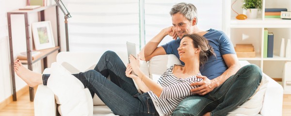 Pár sediaci spolu na sedačke s tabletom v ruke Pár sediaci spolu na sedačke s tabletom v ruke