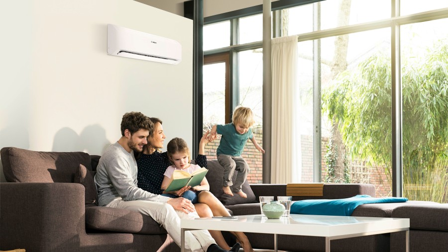 Rodina sediaca na sedačke v obývacej izbe a číta knihu, klimatizácia Bosch inštalovná na stene nad nimi