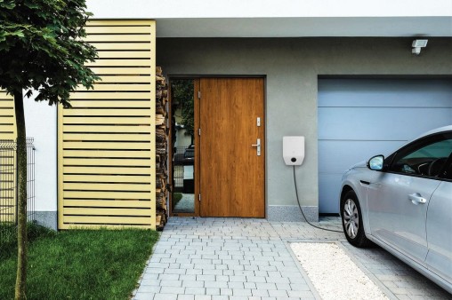 Wallbox Bosch pripevnený medzi vchodovými a garážovými dverami nabíjajúc vonku stojace auto Wallbox Bosch pripevnený medzi vchodovými a garážovými dverami nabíjajúc vonku stojace auto
