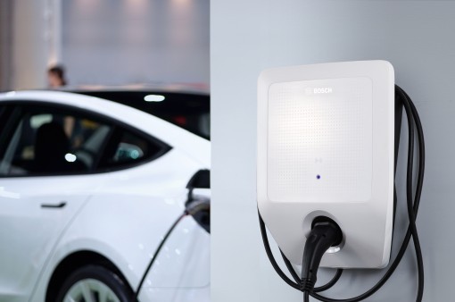 Detail na wallbox Bosch visiaci na stene, biele elektrické auto v pozadí Detail na wallbox Bosch visiaci na stene, biele elektrické auto v pozadí