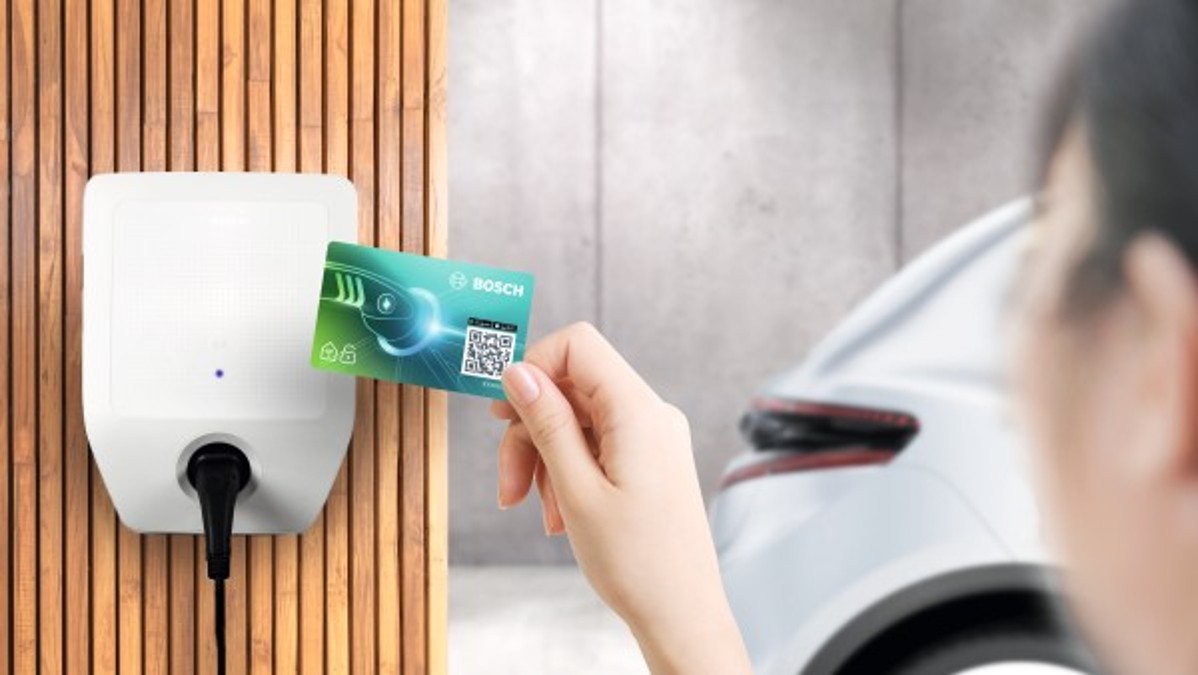 Detail na ruku prikladajúcu RFID kartu k wallboxu Bosch, biele auto v pozadí Detail na ruku prikladajúcu RFID kartu k wallboxu Bosch, biele auto v pozadí