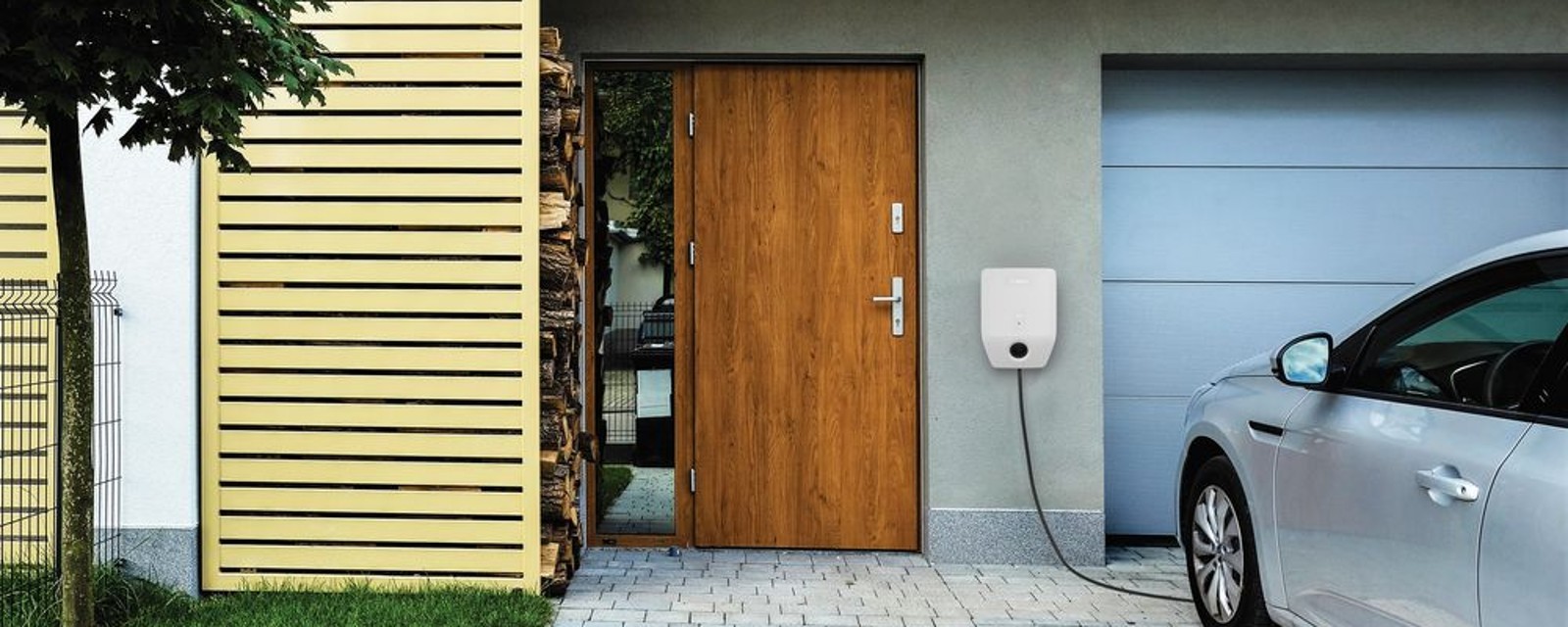Wallbox Bosch pripevnený medzi vchodovými a garážovými dverami nabíjajúc vonku stojace auto Wallbox Bosch pripevnený medzi vchodovými a garážovými dverami nabíjajúc vonku stojace auto