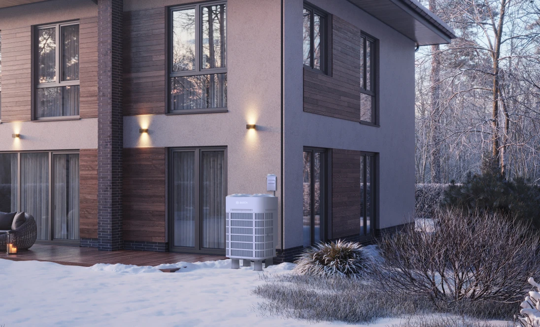 A Bosch IDS Ultra cold climate heat pump sits outside a modern home on a snowy day.