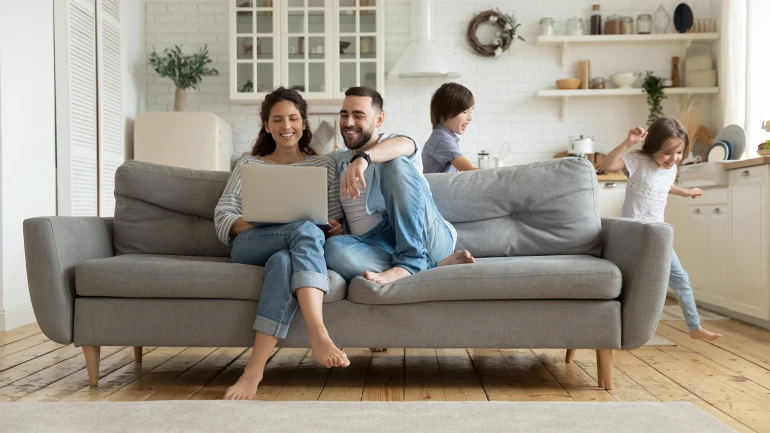 happy couple looking at tablet on couch with children in background