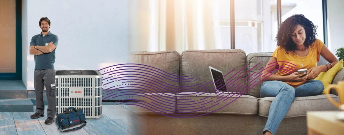 Woman on couch with phone, which is connected via Bluetooth to an IDS Premium Connected heat pump. A contractor is standing next to the unit.