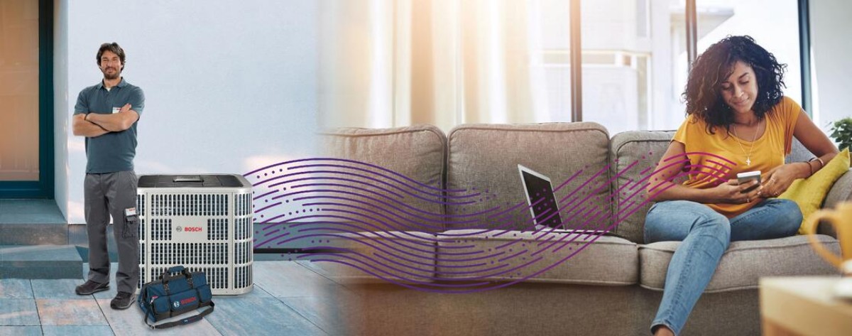 Woman on couch with phone, which is connected via Bluetooth to an IDS Premium Connected heat pump. A contractor is standing next to the unit. Woman on couch with phone, which is connected via Bluetooth to an IDS Premium Connected heat pump. A contractor is standing next to the unit.